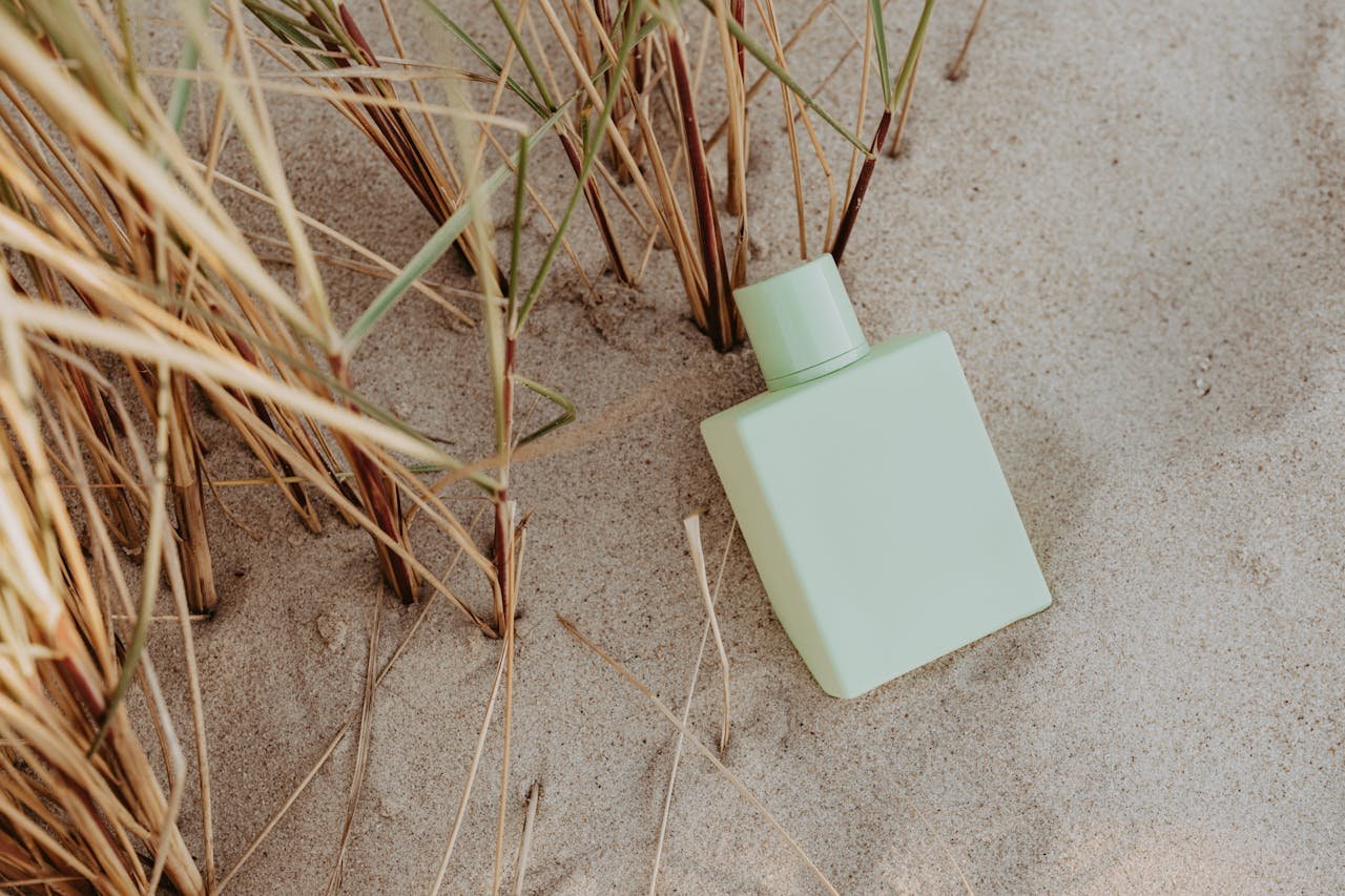 Perfume Bottle on White Sand near Brown Grass